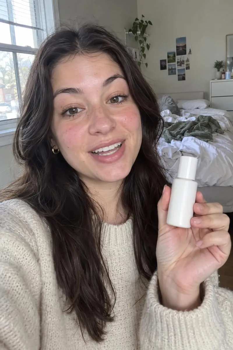 A young woman in her bedroom holds a skincare bottle up to her phone camera and says excitedly: "Okay, this actually changed my skin in a week." Natural window light, casual vibe.